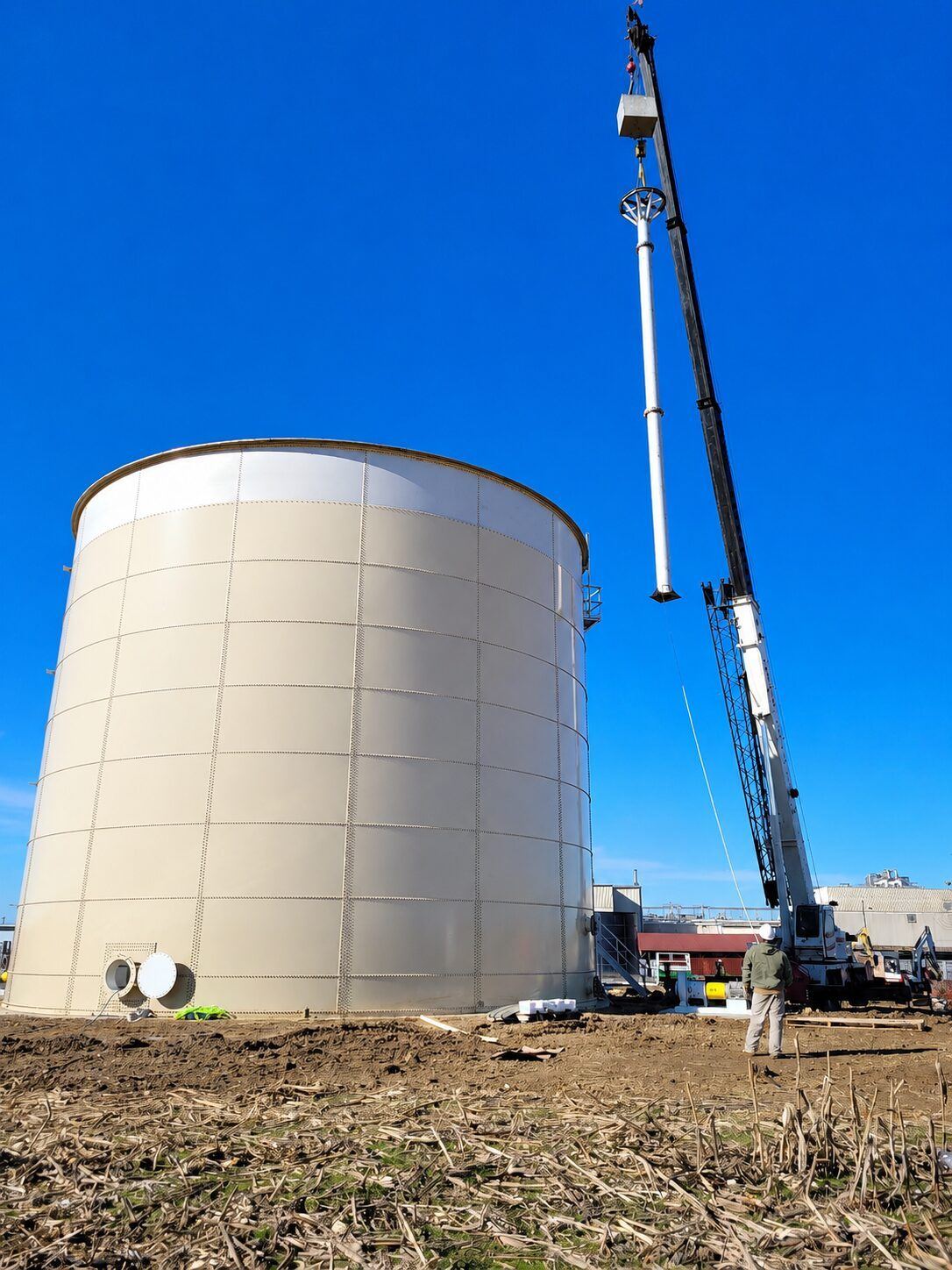 Blue bolted steel tank under construction beside site equipment
