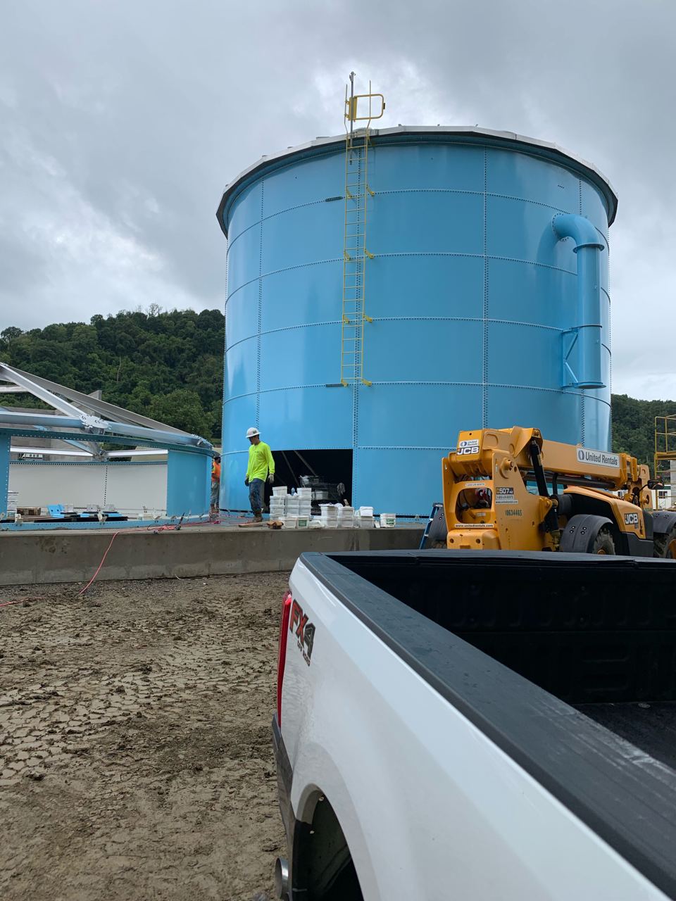 Blue bolted steel tank under construction with a telehandler positioning roof structure