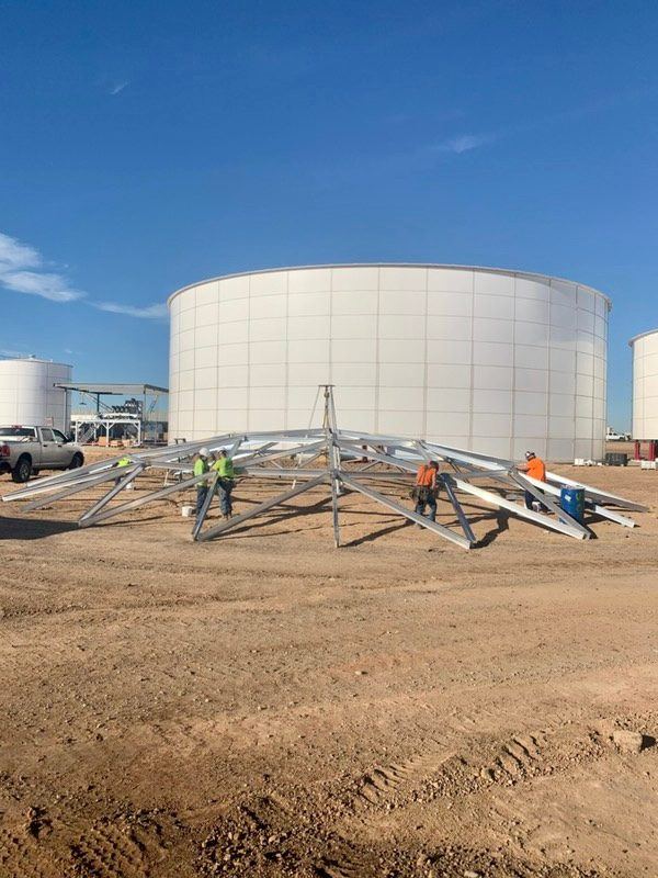 Aluminum dome roof rafters staged on the ground beside a large white bolted steel tank