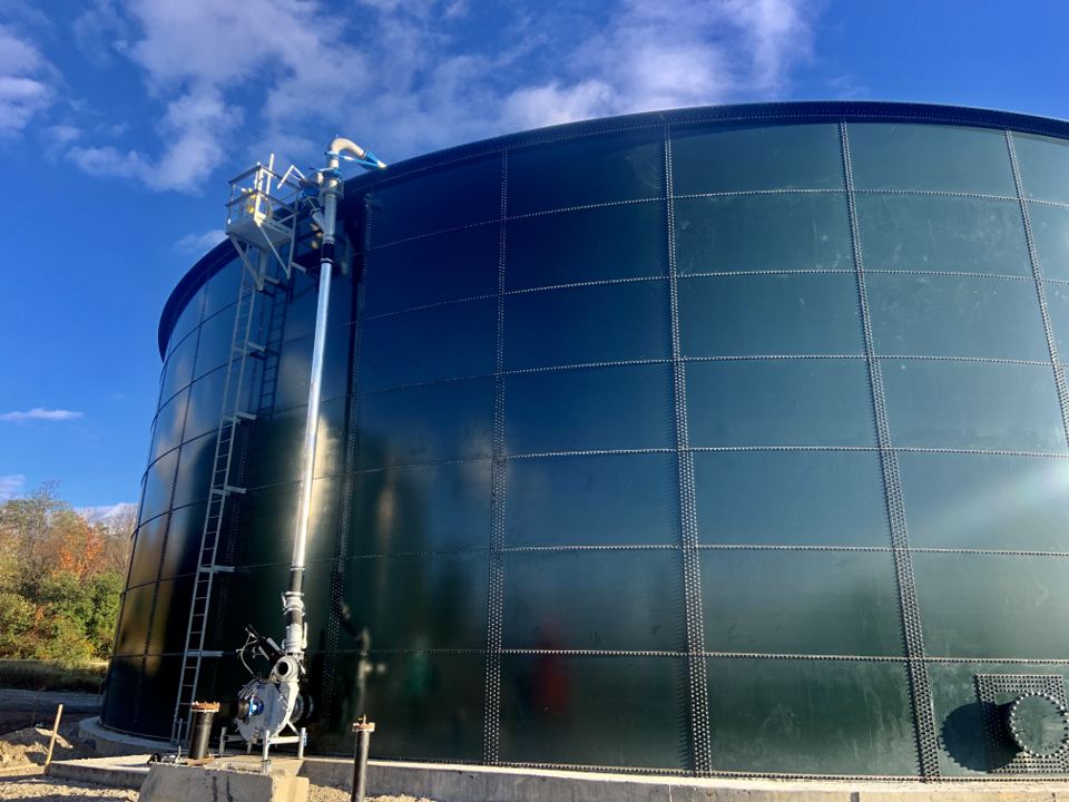 Completed fusion-bonded epoxy bolted steel tank with side-mounted piping against a clear sky