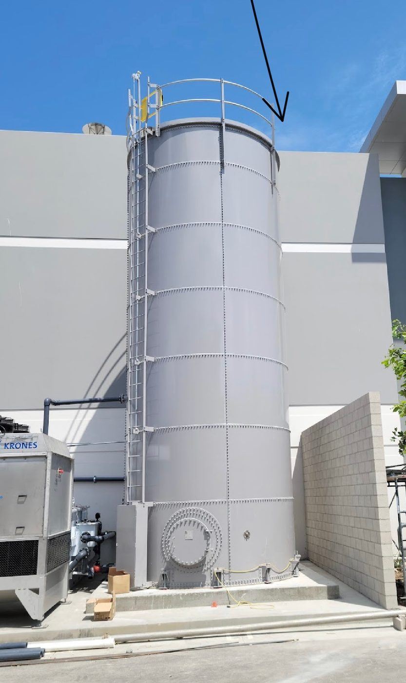 Tall grey bolted steel process tank installed between two industrial buildings