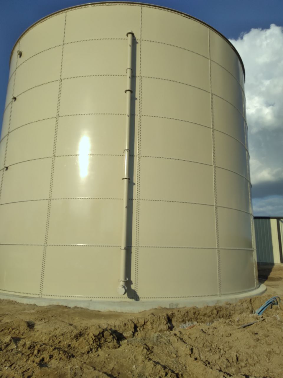 Sunlit tan bolted steel tank shell showing bolted panel seams and exterior ladder