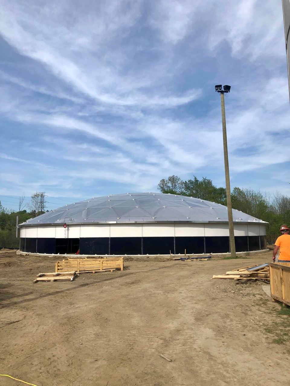 White bolted steel tank with a low aluminum dome roof and blue accent band on a freshly graded site
