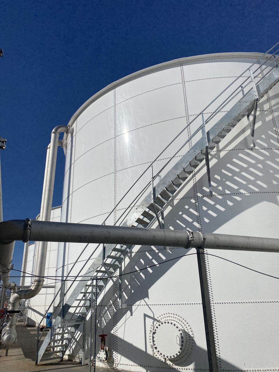 Upward view of a white bolted steel tank shell and roof against a deep blue sky
