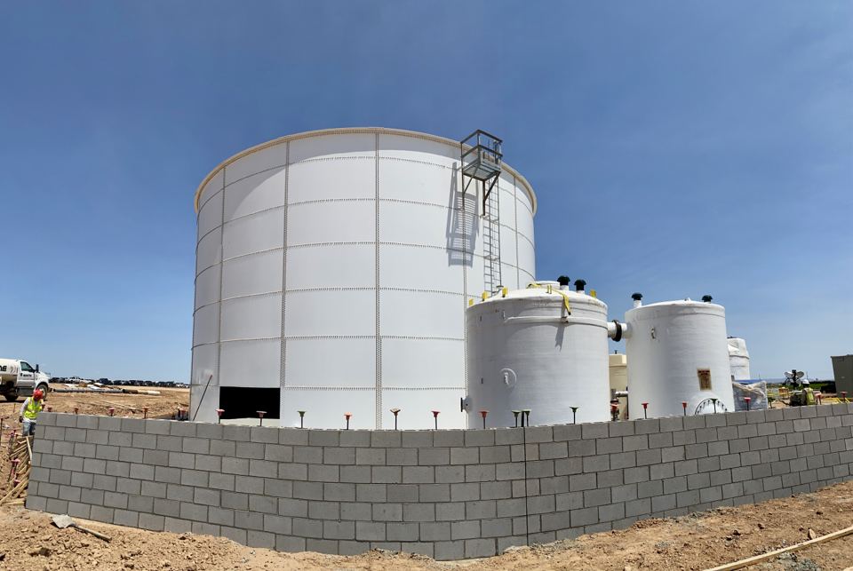 White bolted steel tank behind a block containment wall with process vessels alongside