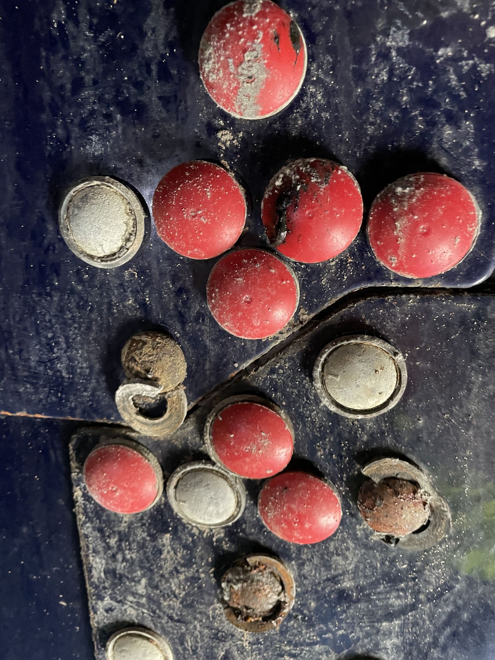Red bolt-cap covers on a tank panel with several caps missing and fasteners corroded