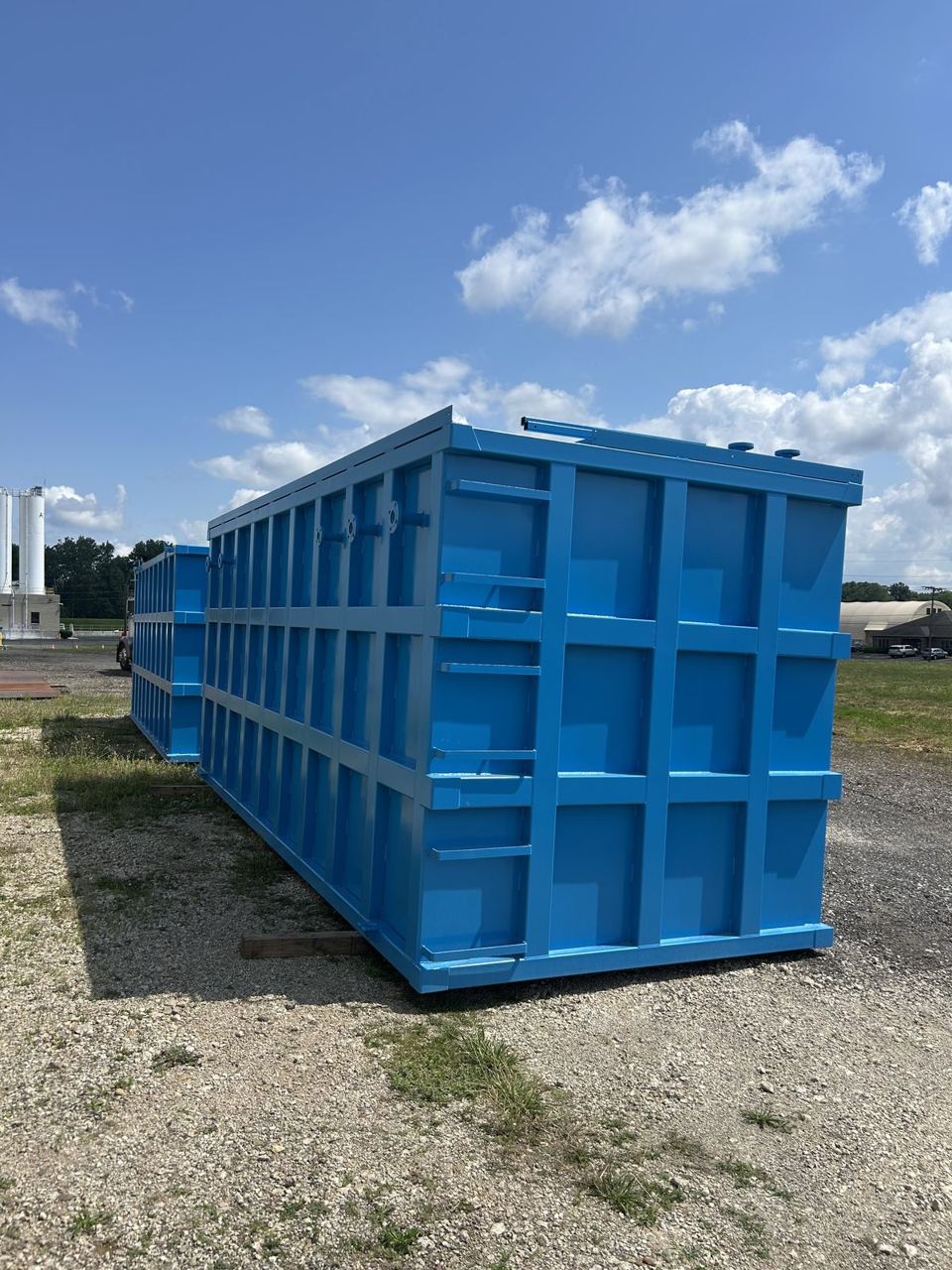 Long bright blue shop-welded steel tank in three-quarter perspective with top-edge nozzles and a reinforced panel grid running its full length outdoors