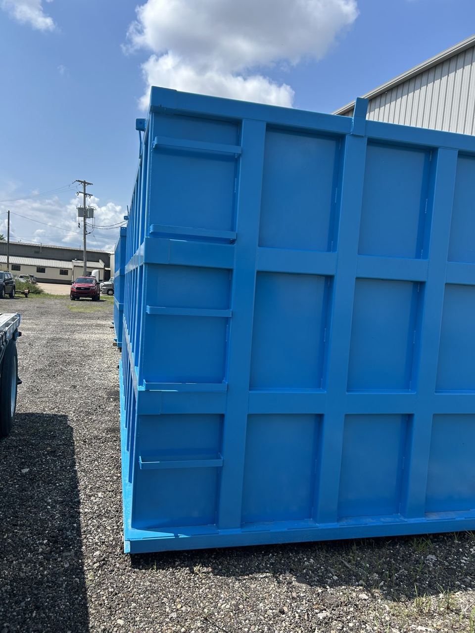 Close-up of the externally reinforced panel grid and welded bracing on the side wall of a bright blue shop-welded steel tank in the yard