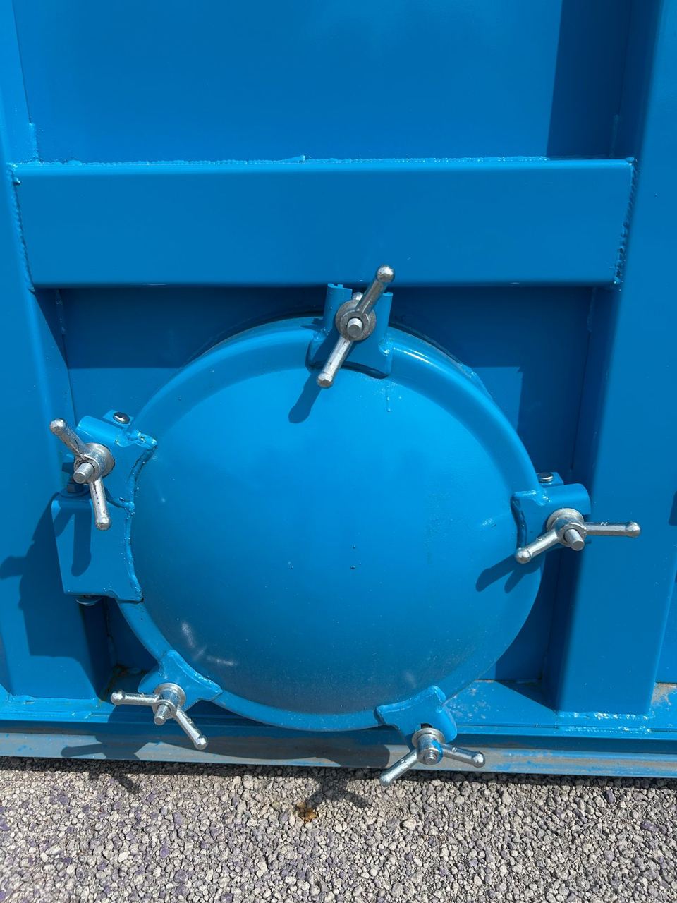 Close-up of a bolted circular manway cover secured with wing-nut clamps on a bright blue shop-welded steel tank in sunlight