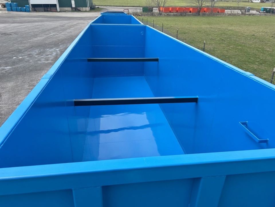 Looking down into the coated interior of an open-top blue shop-welded steel tank with internal baffle bars, staged outdoors