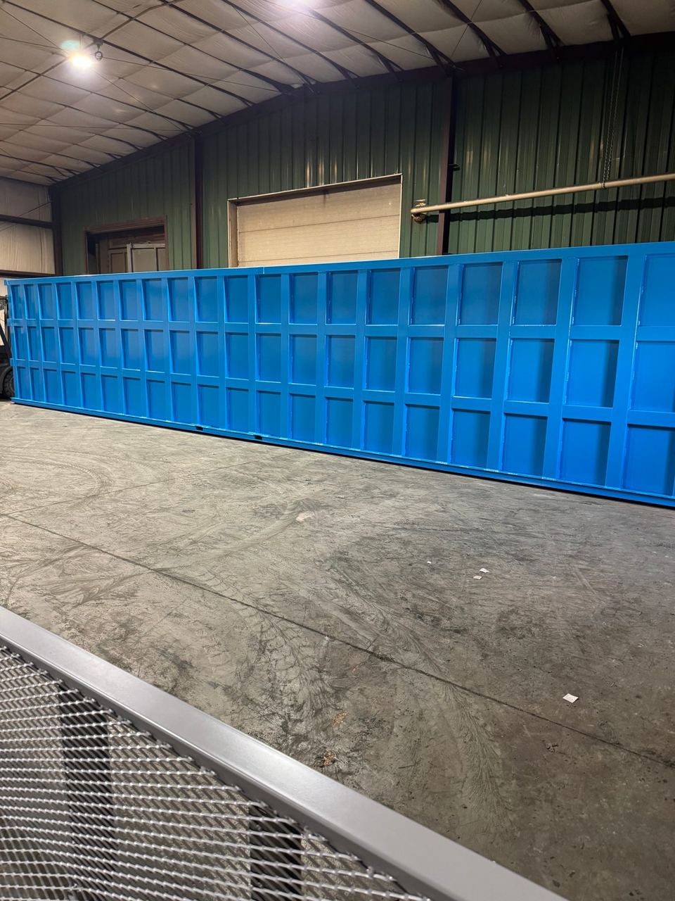 Long low blue shop-welded steel tank in the shop, its full reinforced panel wall facing the camera