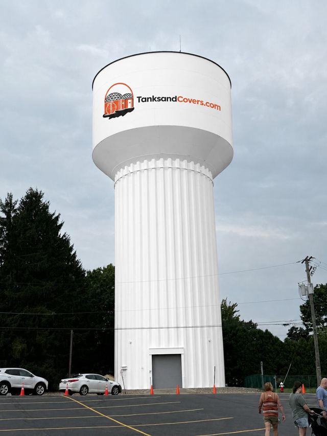 White fluted-column elevated water storage tower branded with the TanksandCovers.com logo