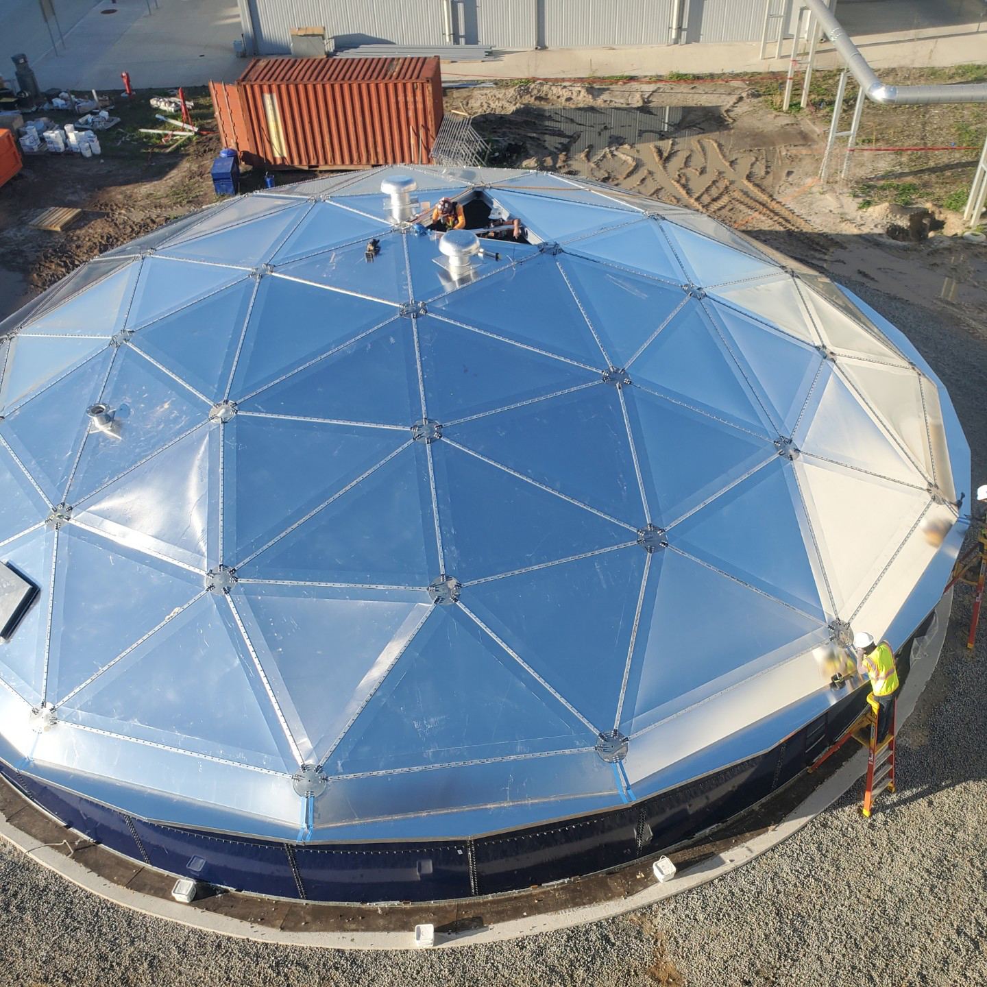 Overhead view of an aluminum dome roof with roof vents, an open access hatch, and crew installing fittings