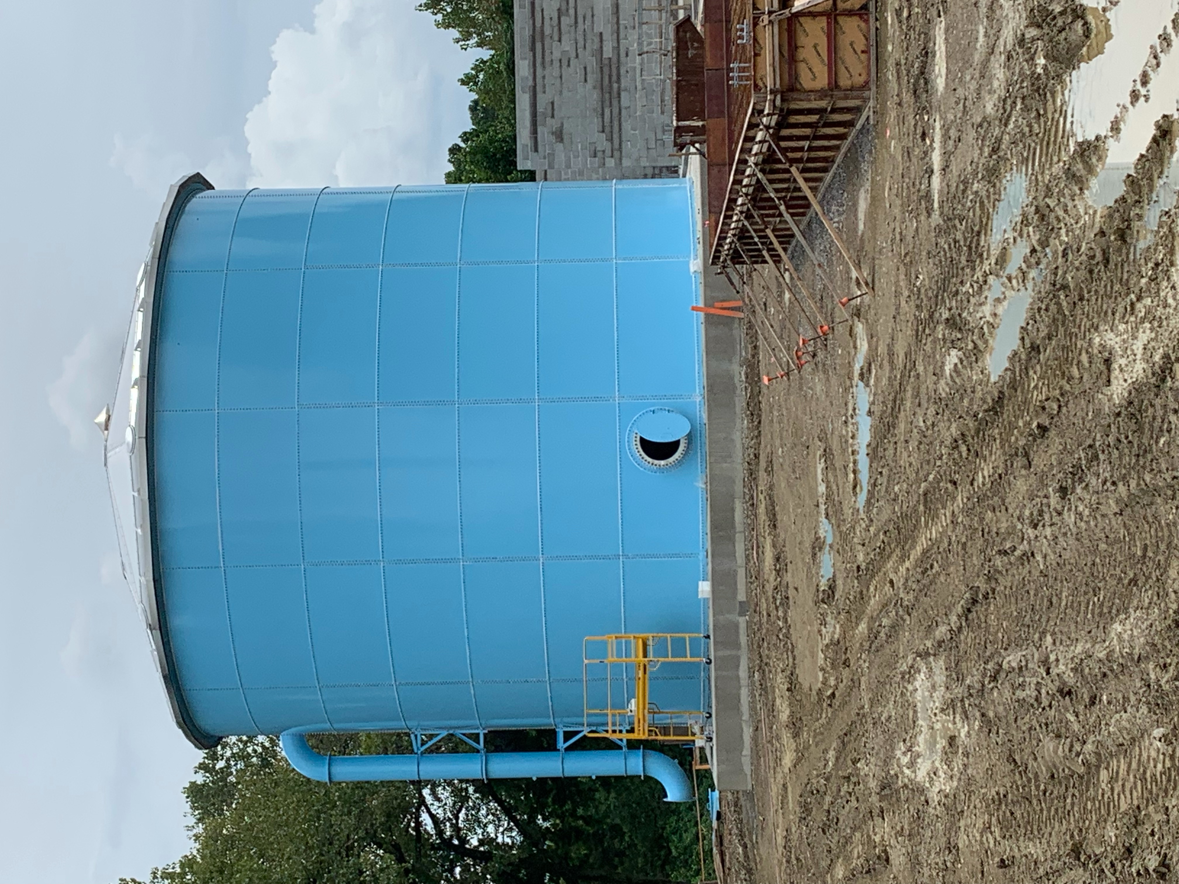 Blue glass-fused-to-steel bolted tank with side manway and inlet piping on a poured ring-wall foundation