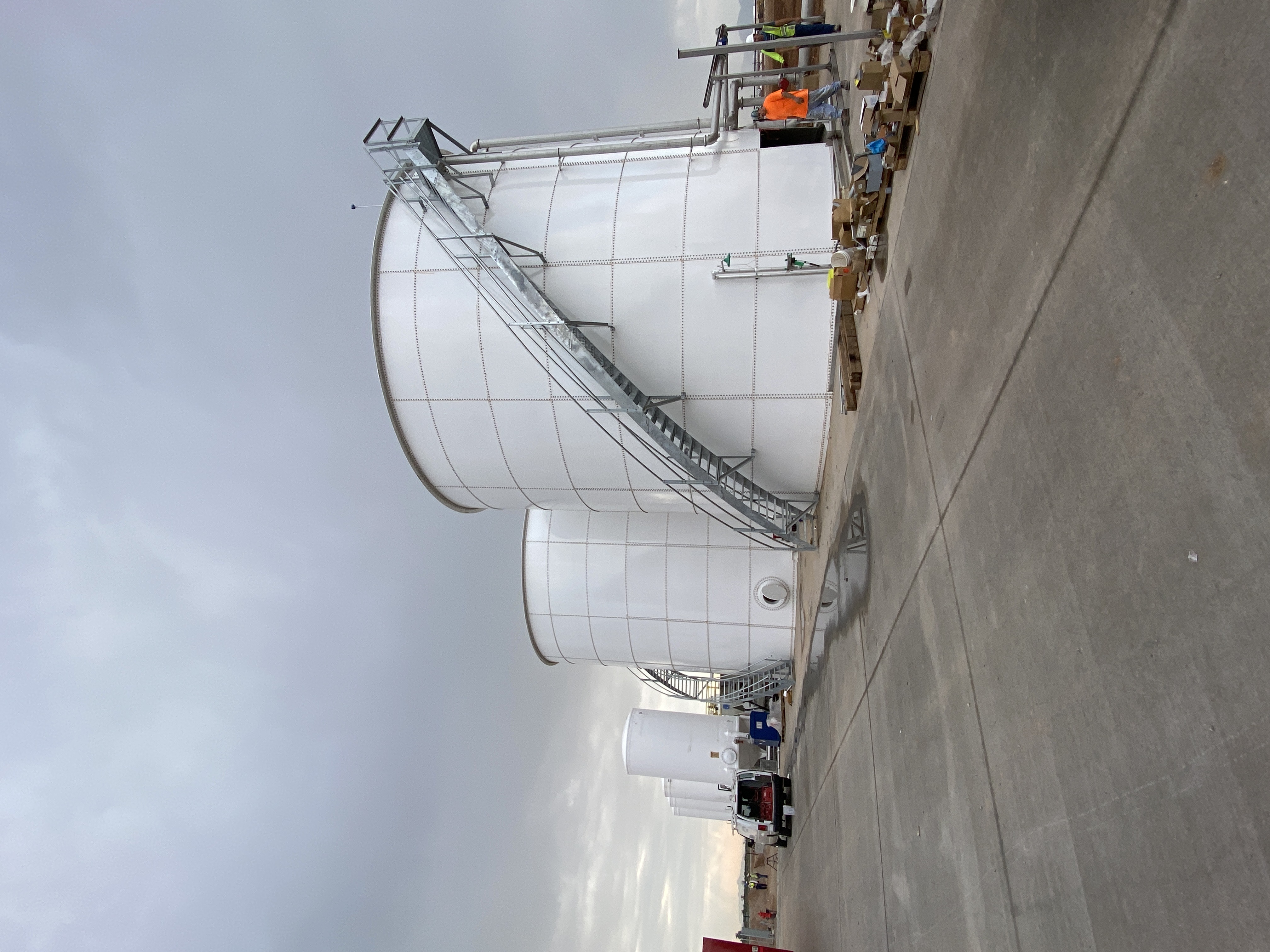 Row of white bolted steel tanks under construction on a paved fabrication yard