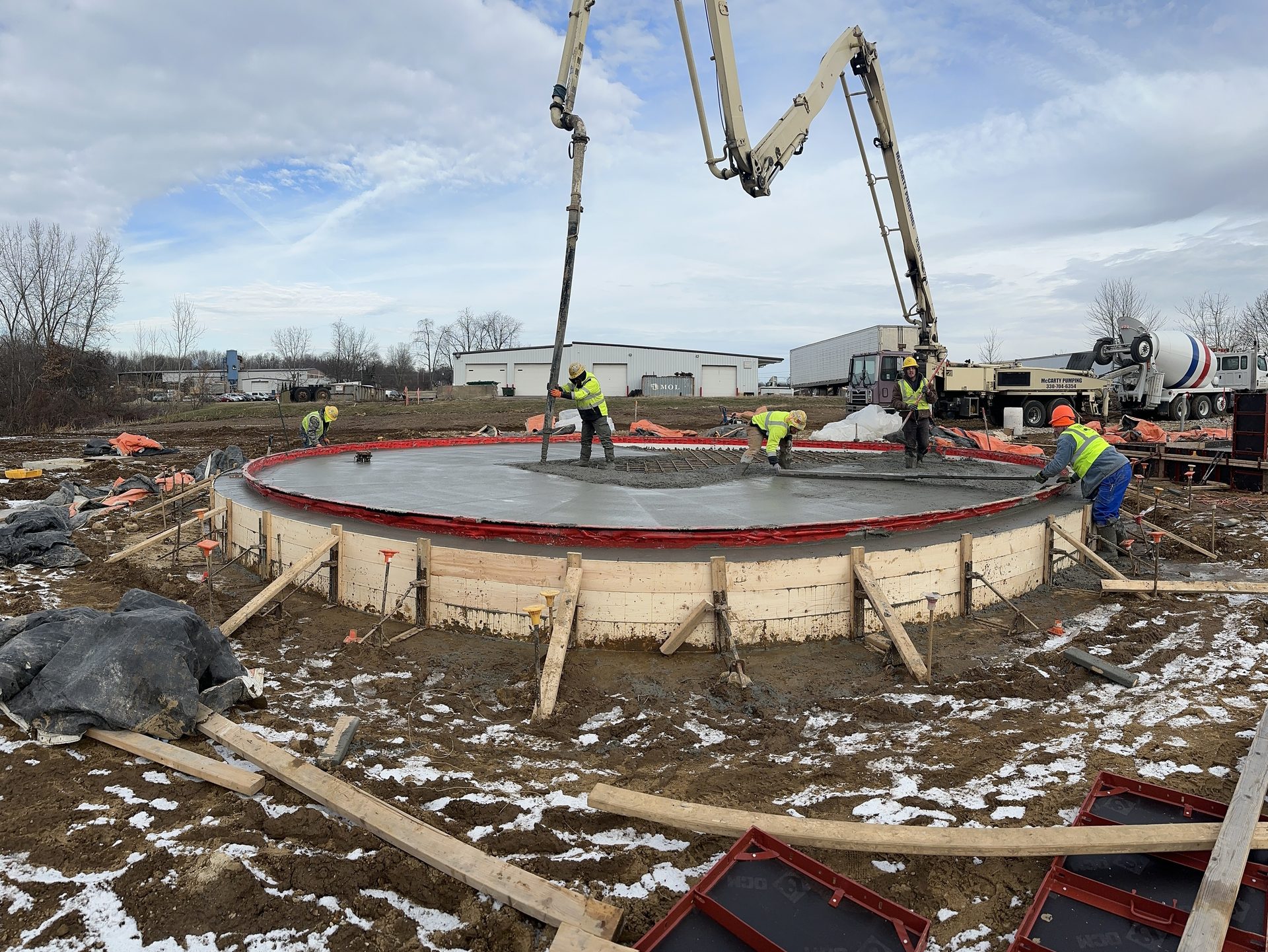 Crew pouring a circular concrete tank foundation with a boom pump