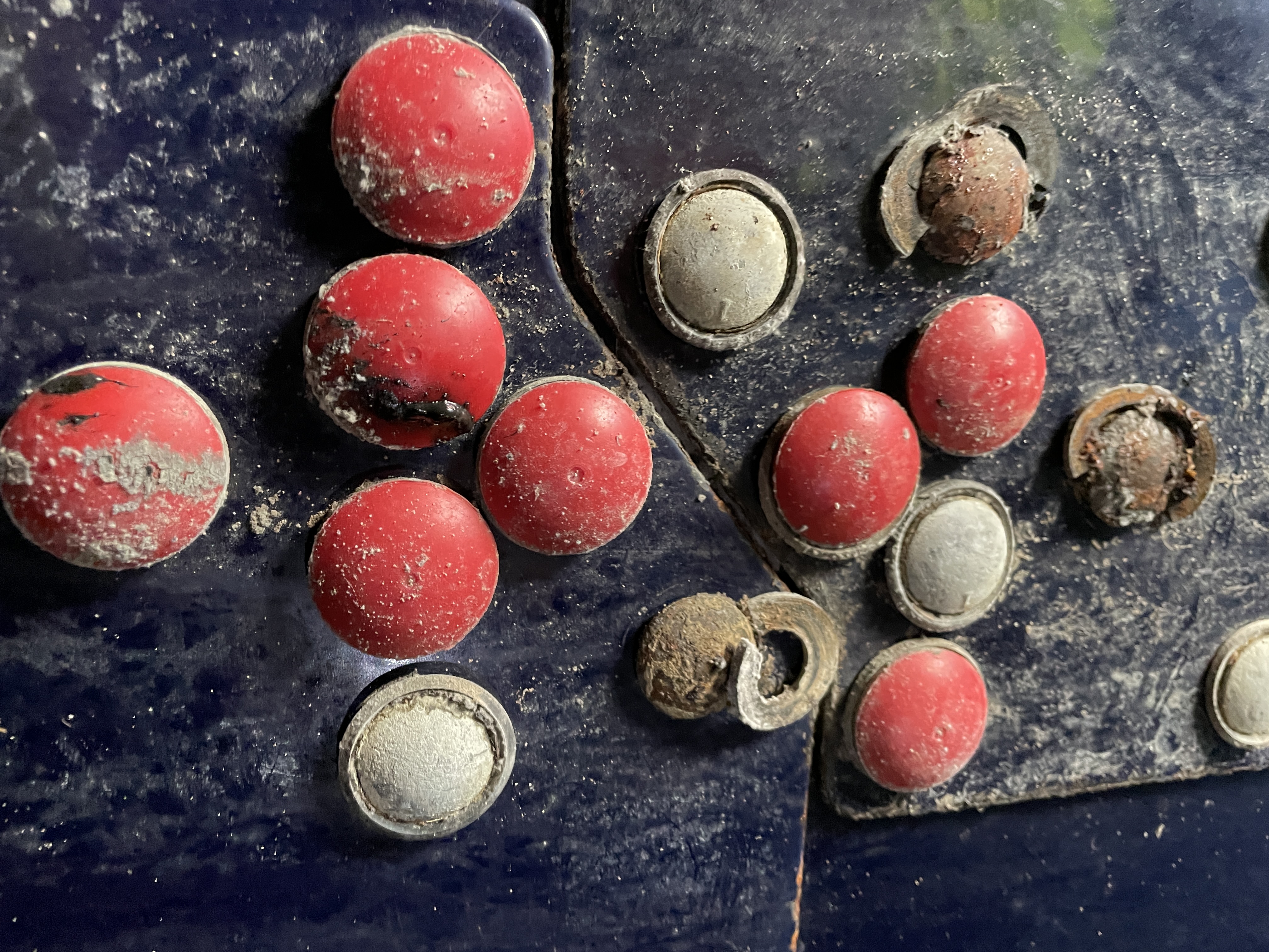 Red bolt-cap covers on a tank panel with several caps missing and fasteners corroded