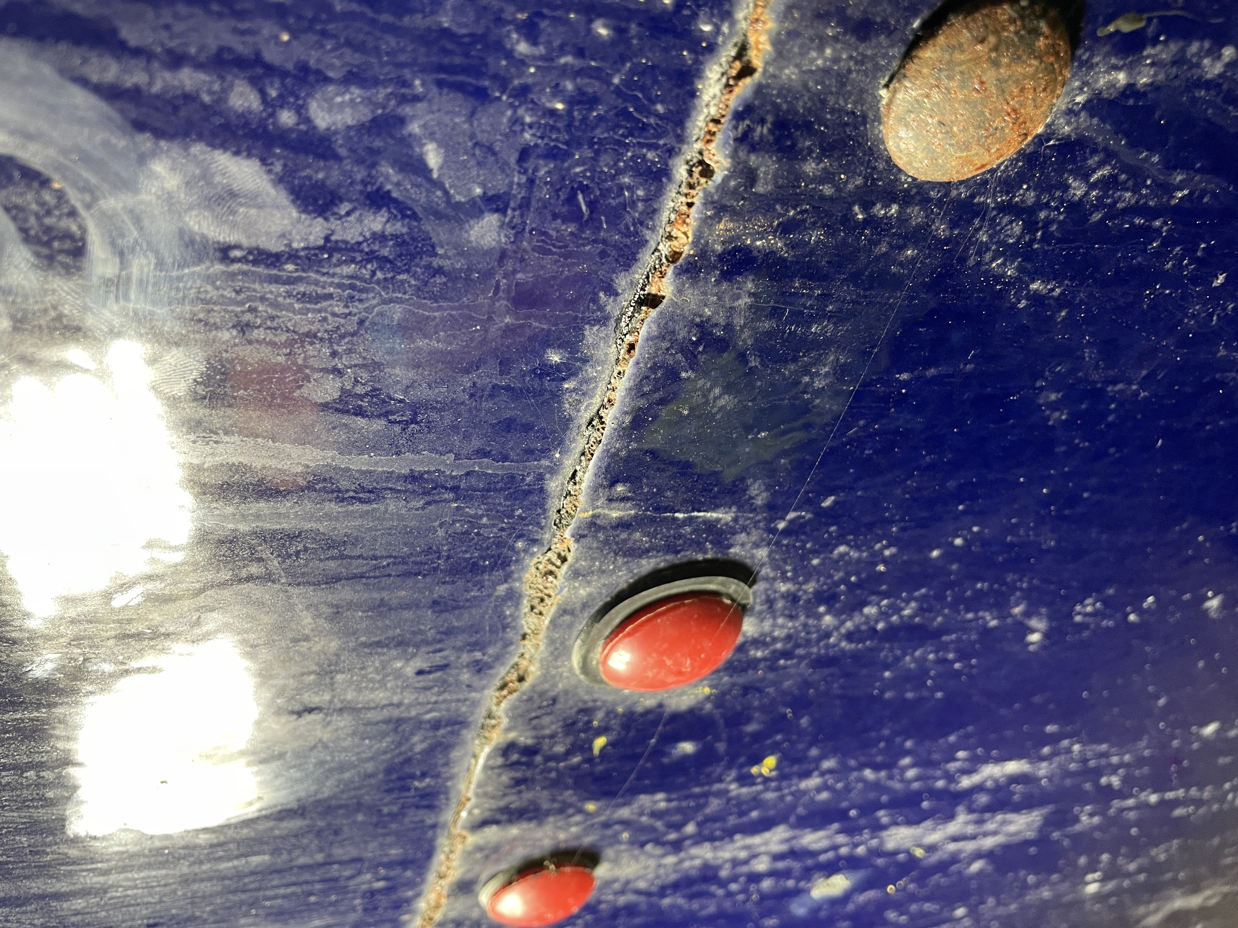 Cracked corroded seam line and bolt cap on a blue coated tank panel