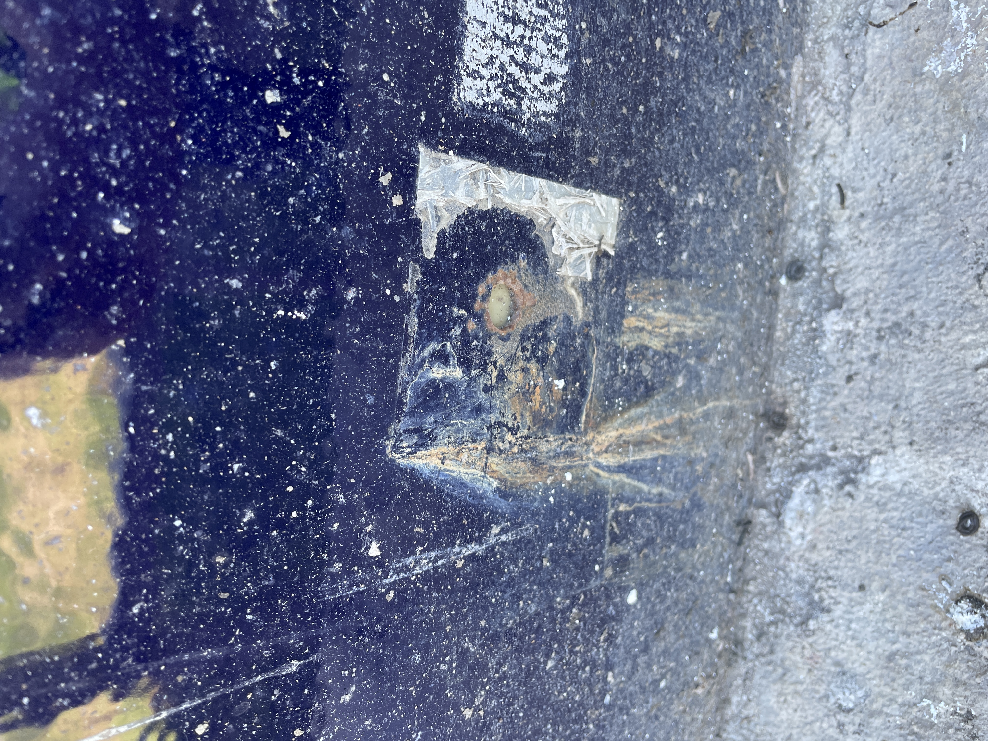 Pitting and corrosion at a tank detail photographed against a concrete surface